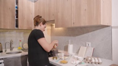 Siyah Tişörtlü Kadın Modern Mutfakta Yumurta Yumurtası Yumurtası Sarısını Beyazdan Ayıran İçindekiler, Açık Yemek Tarifi Kitabı ve Yemek Utensilleri, Ilık Işıklandırma