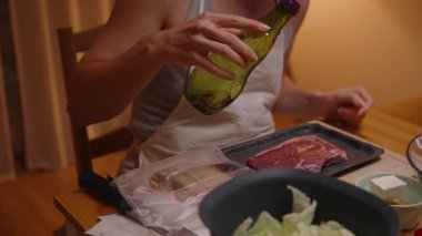 Mutfakta çiğ bifteğe zeytinyağı döken kadın. İçindekiler masanın üstünde.