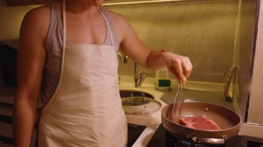 Gaz ocağında çiğ biftek pişirirken elinde maşa tutan kadın.