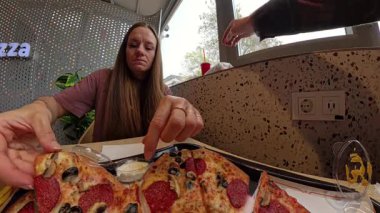 Pizza dilimleyen ve bir restoranda bir tepsi pizza ve sosla otururken bir ısırık alan uzun saçlı kadın ilk insan perspektifinden yakalandı.