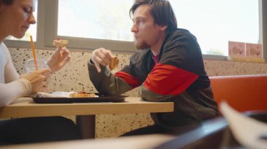Bir restoranda oturan erkek ve kadın birbirlerine bakarken pizza yiyorlar, pizza kabukları tutuyorlar ve sohbet ediyorlar.