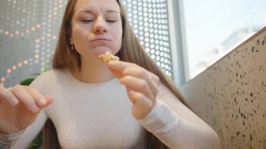 Beyaz kazaklı bir kadın restoranda bir tepsi dilimle otururken peynirli pizzadan bir ısırık alıyor.