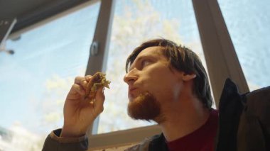 Arka planda Büyük Pencere ile Yukarı Bakarken Bir Sandviç Isıran Adam Düşük Açılı Bakış Açısı