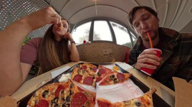 Bir tepsi biberli pizzayla restoranda oturan erkek ve kadın, eline yaslanan kadın ve kamışla soda içen adam, geniş açılı mercekle yakalanan adam.