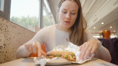 Restoran masasında otururken beyaz kazaklı bir kadın yanında Marul ve peynirle ızgara sandviçten büyük bir ısırık alıyor.