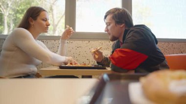 Kadın ve Erkek Restoran Masasında Oturuyor Birbirlerine bakarken Pizza yiyorlar, Ekmek rulosu ile Bulanık Önplan, Arkaplanda Parlak Pencere Işığı