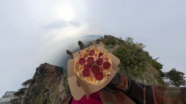 360 derecelik Bozuk Kamera Efektiyle Deniz kenarındaki Yüksek Kayalık Kayalıklarda yürürken Açık Kutuda Pepperoni Pizza taşıyan Bir Adam Görünümü