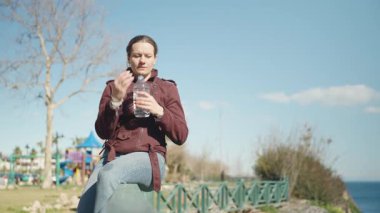 Arka planda Parkta ve Bahçede Parkta Otururken Şişeden Su İçen Bir Kadının Yakın Çekimi