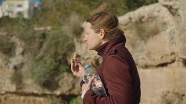 Bir ısırık alırken elinde donut ve bir şişe su tutan Rocky Cliff 'in yanında duran kadın.