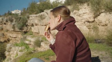 Arka planda Yeşil Çimen ve Rocky Manzaralı Donutu Isıran Bir Kadının Yakın Çekimi