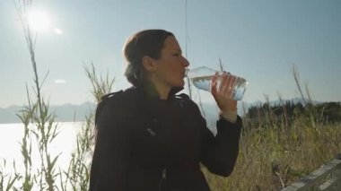 Plastik bir şişeden su içen kadın güneş ışığıyla sıvıyı yansıtıyor.