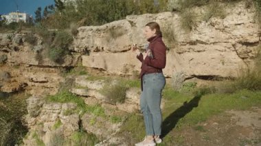 Uçurumun kenarında duran bir kadın su şişesini tutarken donut yiyor.