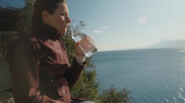 Plastik bir şişeden su içen kadın güneş ışığı yüzeyde yansıyor.