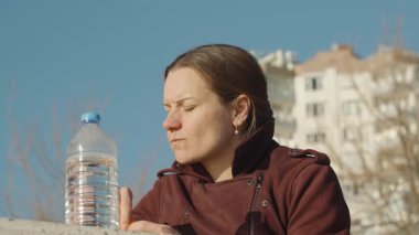 Portakal Dilimleyen Kadın Yanında Su Şişesi, Güneş Işığı Yüzü ve Arkaplanı Aydınlatan Şehir Binaları