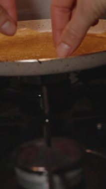 Dikey video. İki eliyle gaz sobasındaki yapışmaz tavadan altın sarısı krep kaldıran kadın.