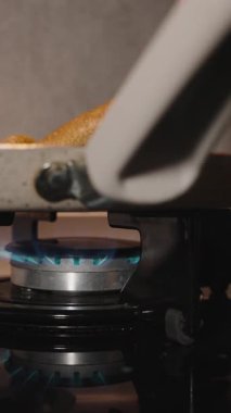 Dikey video. Mavi Gaz Alevi 'nin Üzerinde Yapışkan Olmayan Tavada İnce Çıtır Krepi Çevirmek için Tahta Spatula Kullanmak