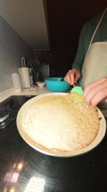 Dikey video. Benzin ocağında Silikonlu Spatula ile Altın Kahverengi Krep Çeviren Kadın