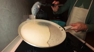 Bir kepçeden bir kepçeye krep hamuru döken kadın Benzin ocağının üzerine bile serpiştirilmiş.