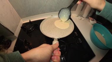 Bir kadının, bir kepçeden tutacağı tutarken yapışmaz tavaya krep hamuru döken ilk kişi görüntüsü.