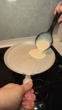 Dikey video. Bir kadının, bir kepçeden tutacağı tutarken yapışmaz tavaya krep hamuru döken ilk kişi görüntüsü.