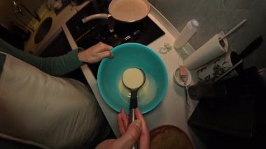 Bir kadının, bir Ladle 'dan gaz sobasındaki yapışmaz tavaya dökülen krep hamuru manzarası