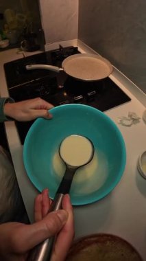 Dikey video. Bir kadının, bir Ladle 'dan gaz sobasındaki yapışmaz tavaya dökülen krep hamuru manzarası