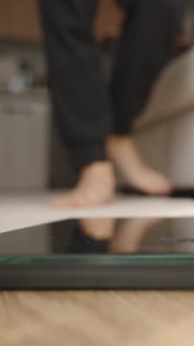 Dikey video. Yalın Ayaklı Kişi Ev Ayarlarında Tahta Döşeme Üzerinde Dijital Ölçekte Adımlıyor