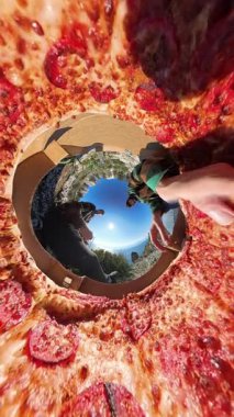 Dikey video. Bir Açık Kutudan Pizza Dilimlerine Erişen İki Kişi 360 derecelik Ufacık Gezegen Efekti ile yakalanmış, Manzaralı Eşsiz bir Perspektif ve Parlak Mavi Gökyüzü