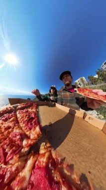 Dikey video. Erkek ve Kadın Pepperoni Pizza Dilimlerini Açık Kutudan Parlak Güneş Altında Eşsiz Geniş Açı Bakış Alanından Çekiyor.