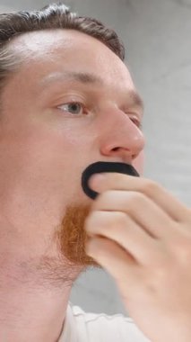 Dikey video. Siyah Ağız Bandını Ayna 'ya Bakarken Kaldıran ve Yakın Çekimde Gözünü Kıstıran Adam Uyku Terapisi Konseptinden Direnç Gösteriyor