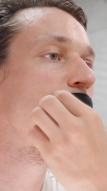 Dikey video. Aynanın Önündeki Adam Gece Soluk Alma Terapisi İçin Odaklı İfadeyle Siyah Ağız Bandını Kaldırıyor