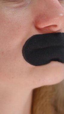 Dikey video. Yapışkan Kavram 'dan rahatsızlık gösteren Dudaklardan Siyah Ağız Bandını Çıkartırken Yüzü Surat Atan Kadın