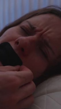 Dikey video. Yataktaki Kadın, Uyku Rahatsızlığı Konsepti İçin Uykusuz Kalmadan Önce Solunabilir Ağız Bandını Gözleriyle Kapalı Tutarken Hayal Kırıklığına Uğradı