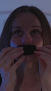 Dikey video. Gece Uykusuna Hazırlık Konsepti için Yatakta Oturan Kadın Ağzına Bant Bantla İki Elinle Loş Mavi Işıkta