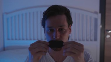 Gece Yatağında Oturan Adam Gece Solunumu Geliştirme Konsepti için Mavi Ortam Işığı Altında Uyumadan Önce Ağız Bandı Uyutuyor