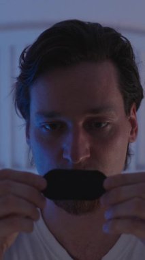 Dikey video. Gece Yatağında Oturan Adam Gece Solunumu Geliştirme Konsepti için Mavi Ortam Işığı Altında Uyumadan Önce Ağız Bandı Uyutuyor