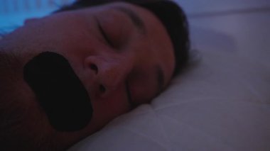 Uyku Bozukluğu Konsepti 'ne Uykuya dalmadan önce Kapalı Işık Altında Sinirli İfadesiyle Yatakta Uyanan Adam Sinir bozucu Ağız Bandını Kaldırıyor