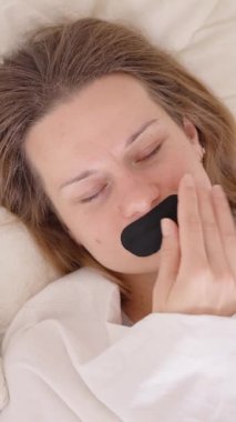 Dikey video. Parlak Uyku Yardımı Değerlendirme Odasında Yapışkan Rahatsızlıktan Tereddüt Ederken Bir Kadın Uyanıp Ağız Bandını Çıkartıyor