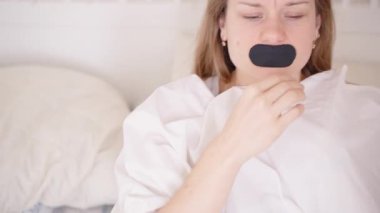 Ağız bandını çıkardıktan sonra Gözler Kapalı ve Sabah Uykusu İçin Omuzlar Örtülü Kadın Uyanıp Yataktan Kalkıyor