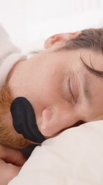 Dikey video. Yatakta yatan adam ağzı bantla kapatır gözleri kapalı ve acı dolu bir ifadeyle uykusuzluktan uyur uykusuzluktan.