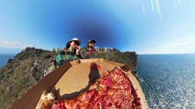 Erkek ve Kadın Uçurumun kenarında Pizzanın Tadını Çıkarırken, Önde Açık Kutu, Geniş Açı Mercek ve Çarpıcı Kıyı Manzarası ile Yakalandı.