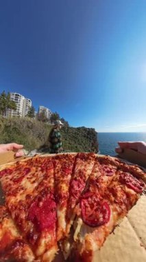 Dikey video. Bir Kadın Arkaplanda Sahne Görünümünü İzlerken Açık Kutudan Pizza Dilimlemek İçin İki El Uzanıyor