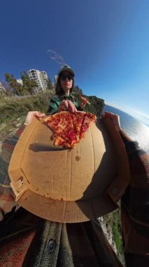 Dikey video. Ufacık Gezegen Efektli Açık Pizza Kutusu Tutan, Okyanus ve Şehir Arkaplanı ile Eşsiz 360 derecelik Bakış Açısı Yaratan