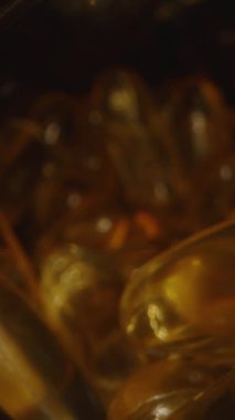 Dikey video. Dolly Kamera Kaydırıcısı Omega 3 kapsüllerinden oluşan bir kavanozdan çıkıyor, Siyah Arkaplan 'daki ışığı yansıtan Şeffaf Gel Kapsüllerinin yakın çekim görüntüsüyle Macro' yu Karanlık bir ayarda çekiyor
