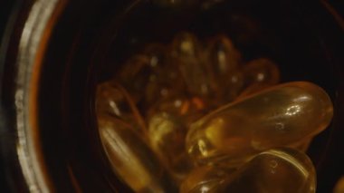 Dolly Kamera Kaydırıcısı Omega 3 kapsüllerinden oluşan bir kavanozdan çıkıyor, Siyah Arkaplan 'daki ışığı yansıtan Şeffaf Gel Kapsüllerinin yakın çekim görüntüsüyle Macro' yu Karanlık bir ayarda çekiyor