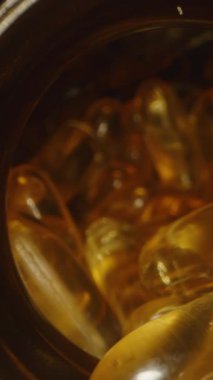 Dikey video. Dolly Kamera, Parmaklar Şişeden Bir Omega 3 Kapsülü Çıkarırken Hareket Ediyor, Saydam Jel Kapsülünün Arka planda Görünür Daha Fazla Kapsüllü Makro Yakın Çekimini Gösteriyor
