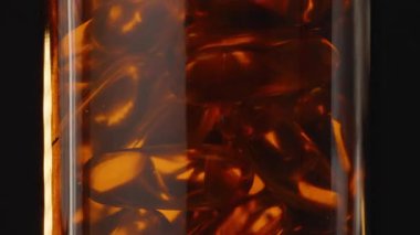 Omega 3 kapsülleriyle dolu Kahverengi Cam Şişe 'nin 360 derecelik Dönüşü Karanlık Arkaplan Karşısındaki Ilık Işığı Yansıtır