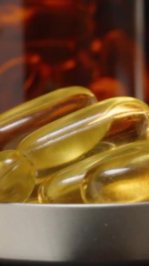Dikey video. Kahverengi bir Cam Şişenin Önünde İçi Omega 3 Kapsülle Dolu Bir Şişe Kapağının 360 derecelik Dönüşü Ilık Işık Yansımalı Karanlık Bir Arkaplana Karşı