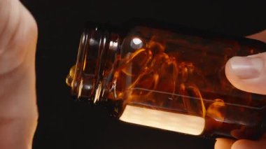 Omega 3 kapsüllerini kahverengi bir cam şişeden açık bir avuç içine dökerek karanlık bir arkaplan yakalama hareketi