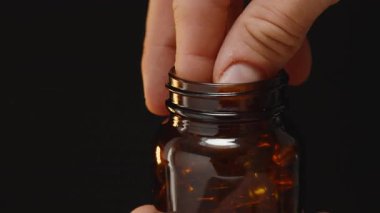 Bir Omega 3 kapsülünü açık boyunla kahverengi bir cam şişeye atıp Karanlık Arkaplan Karşısındaki Hareketi Yakalamak